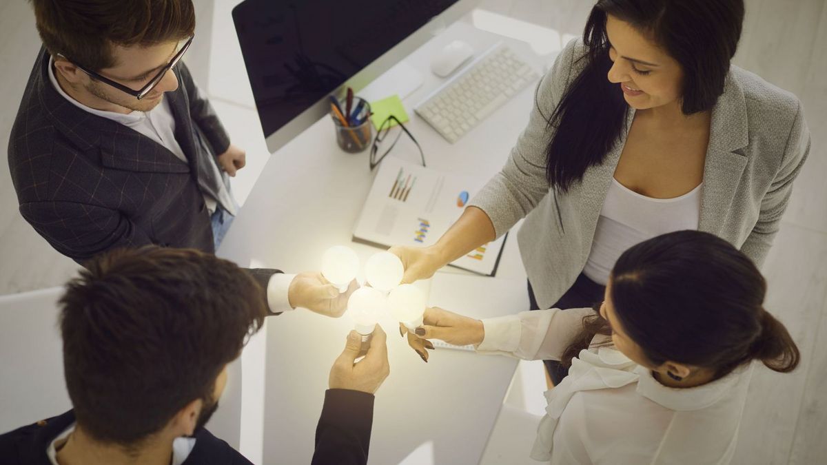 enlarge the image: Four people at a desk holding a lightbulb each