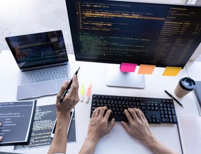 Zwei Menschen an einem Schreibtisch, vor ihnen ein Laptop und ein großer Bildschirm