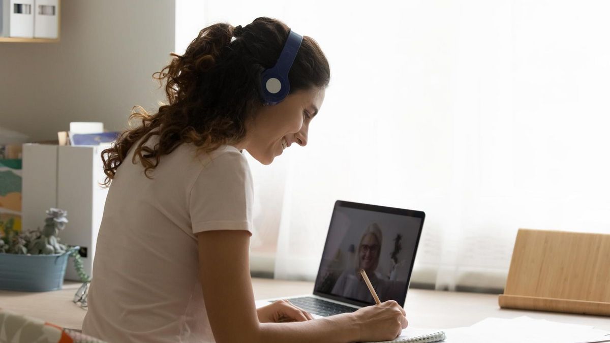 Junge Frau an einem Schreibtisch, auf dem ein Laptop steht. Es läuft ein Videocall.