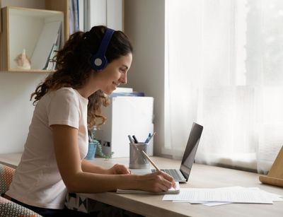 Junge Frau am Schreibtisch, vor ihr ein Laptop und Zettel