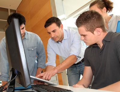 Studierende und ein Dozent vor einem Computer