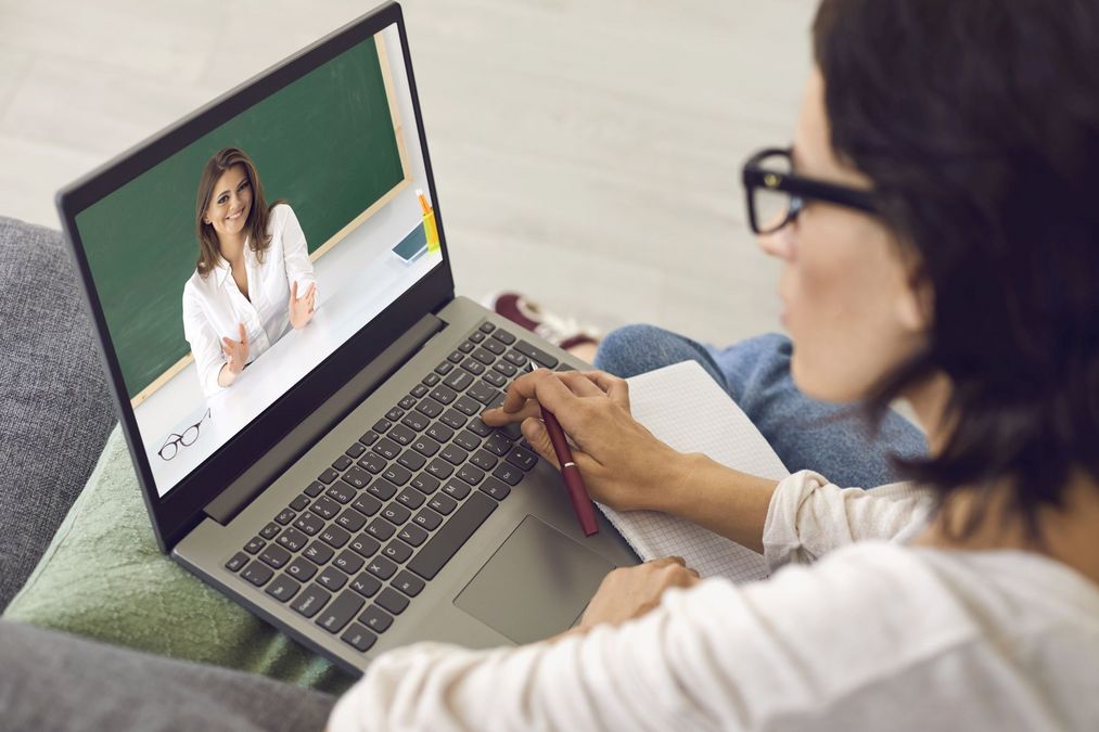 Frau auf einem Sofa sieht ein Lehrvideo auf einem Laptop