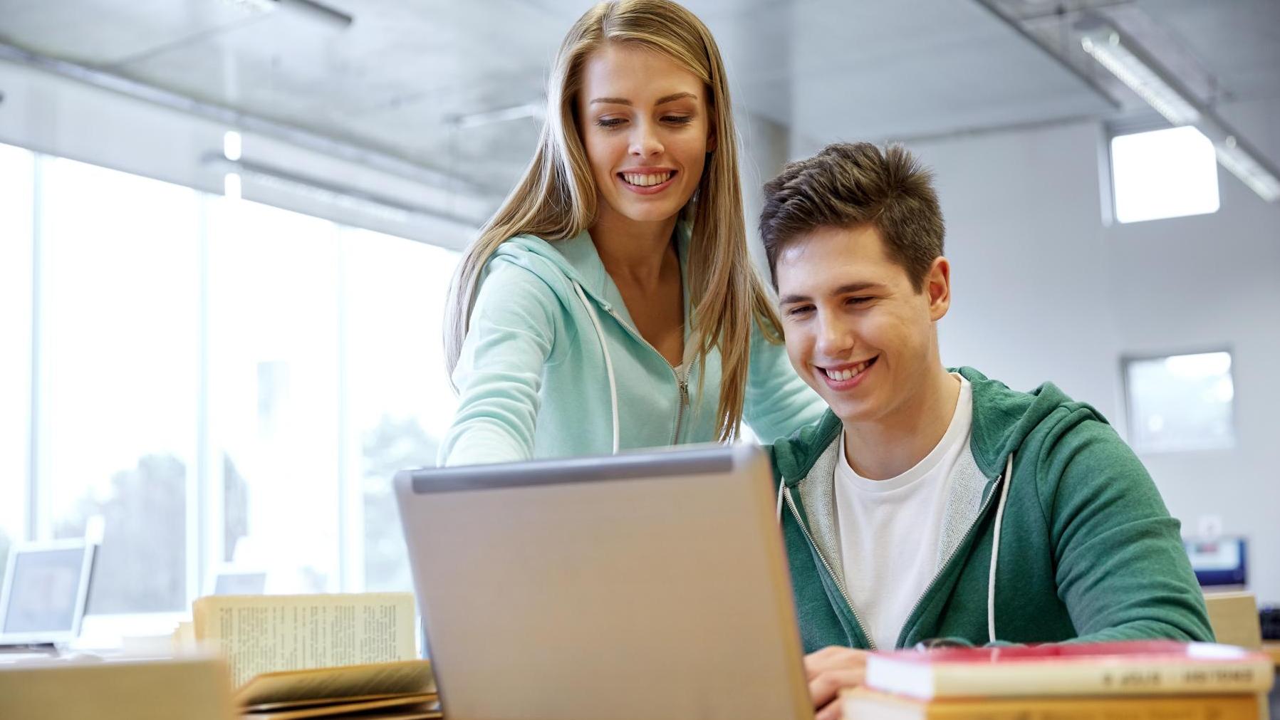 Eine junge Frau und ein junger Mann in einer Bibliothek an einem Laptop