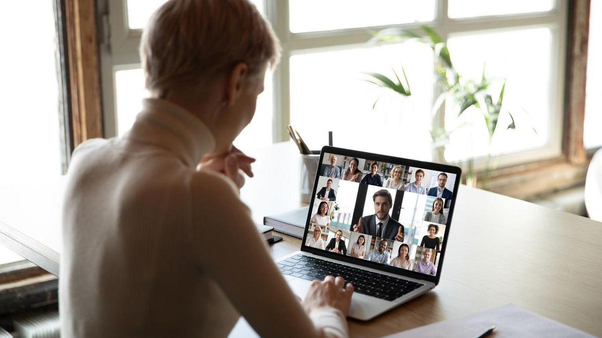 Junge Frau an einem Schreibtisch vor einem Laptop, auf dem eine Videokonferenz läuft.