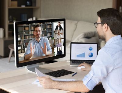 Mann an Schreibtisch in einer Videokonferenz, auf dem Bildschirm andere Personen, die an der Konferenz teilnehmen