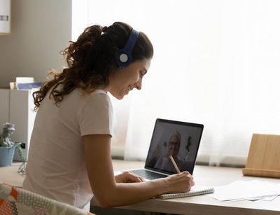 Junge Frau an einem Schreibtisch, auf dem ein Laptop steht. Es läuft ein Videocall.