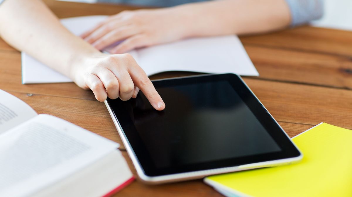 Eine Person sitzt an einem Tisch auf dem ein Tablet liegt