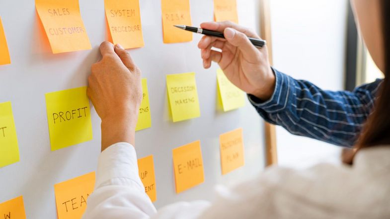 Zwei Menschen zeigen auf Post-it-Zettel an einem Whiteboard