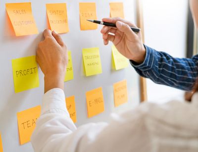 Zwei Menschen zeigen auf Post-it-Zettel an einem Whiteboard